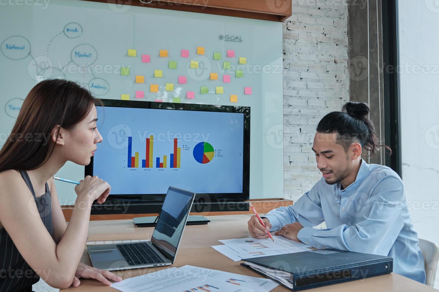 zwei kollegen und mitarbeiter asiatischer ethnizität brainstormen und treffen finanzierungsprojekte diskutieren mit geschäftsdiagrammen in einem konferenzraum mit buntem klebenotizpapier, das im büro an bord geklebt wird. foto