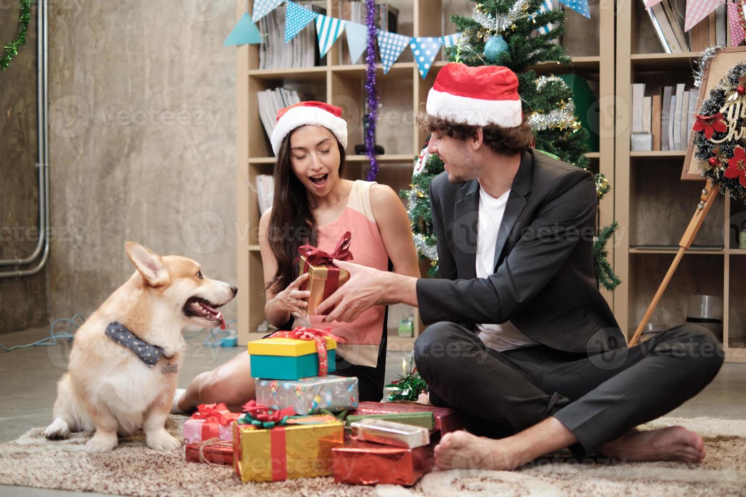 Überraschen Sie zwei Mitarbeiter und einen Hund in der Nähe, indem Sie Geschenke geben, während Sie vor dem Firmenurlaub am Büroarbeitsplatz sprechen, ist für die Weihnachtsfeier und die Neujahrsfeier dekoriert. foto