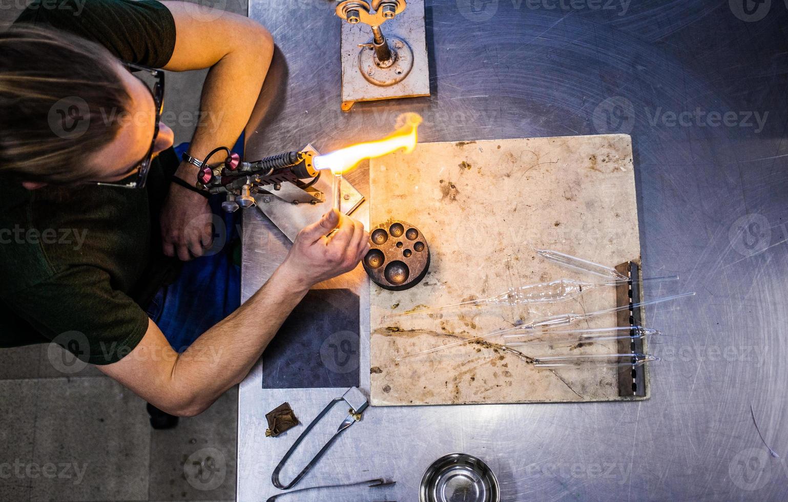 Glasbläser junger Mann, der an einer Fackelflamme mit Glasröhren arbeitet foto