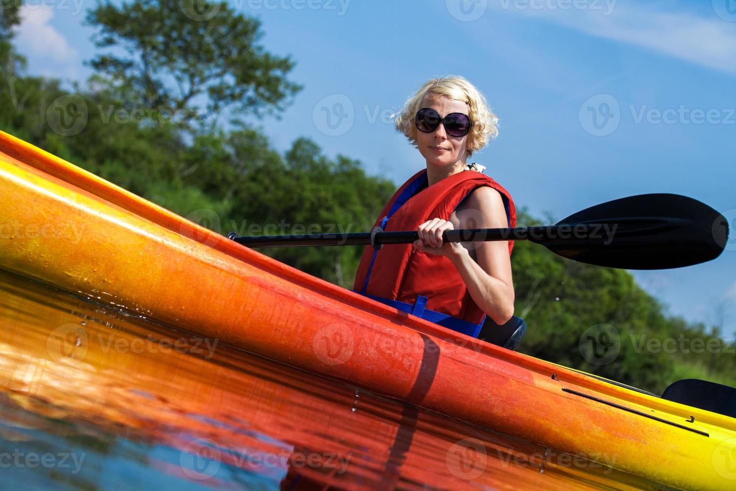 Frau mit Warnweste, die alleine auf einem ruhigen Fluss Kajak fährt foto