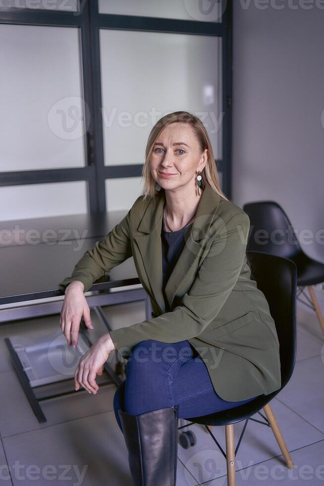 blond Frau mit lange Haar im ein Grün Jacke und Jeans im das Büro foto