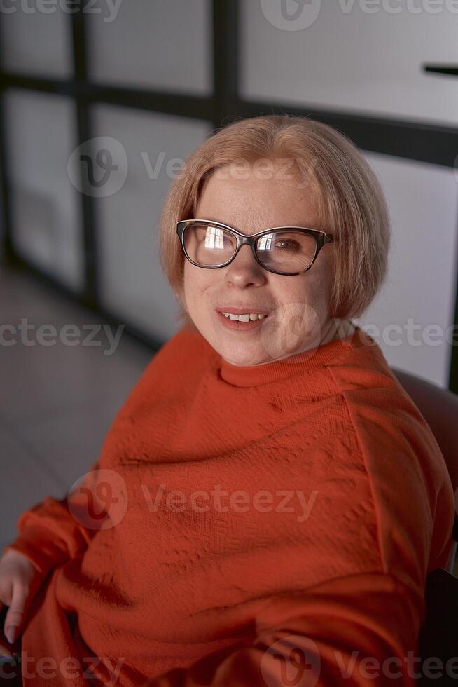 Porträt von ein Frau mit ein Behinderung im ein Orange Sweatshirt und Leder Hose im das Büro foto
