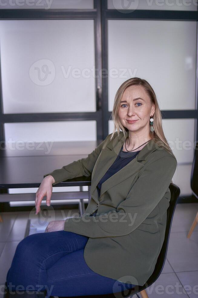 blond Frau mit lange Haar im ein Grün Jacke und Jeans im das Büro foto