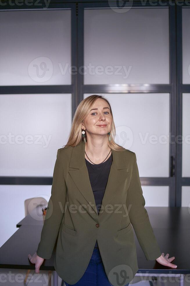 blond Frau mit lange Haar im ein Grün Jacke und Jeans im das Büro foto