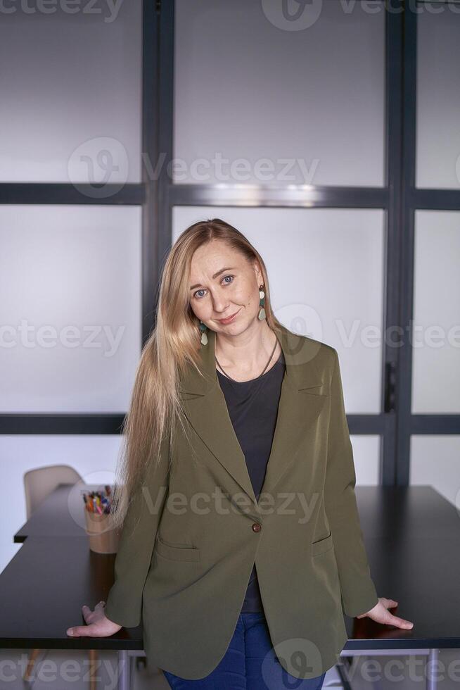 blond Frau mit lange Haar im ein Grün Jacke und Jeans im das Büro foto