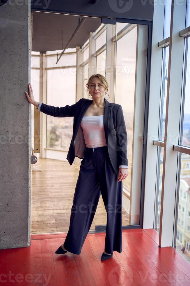 attraktiv Mitte Alter Frau im Jacke und Weiß T-Shirt posieren im modern Büro mit Panorama- Fenster foto