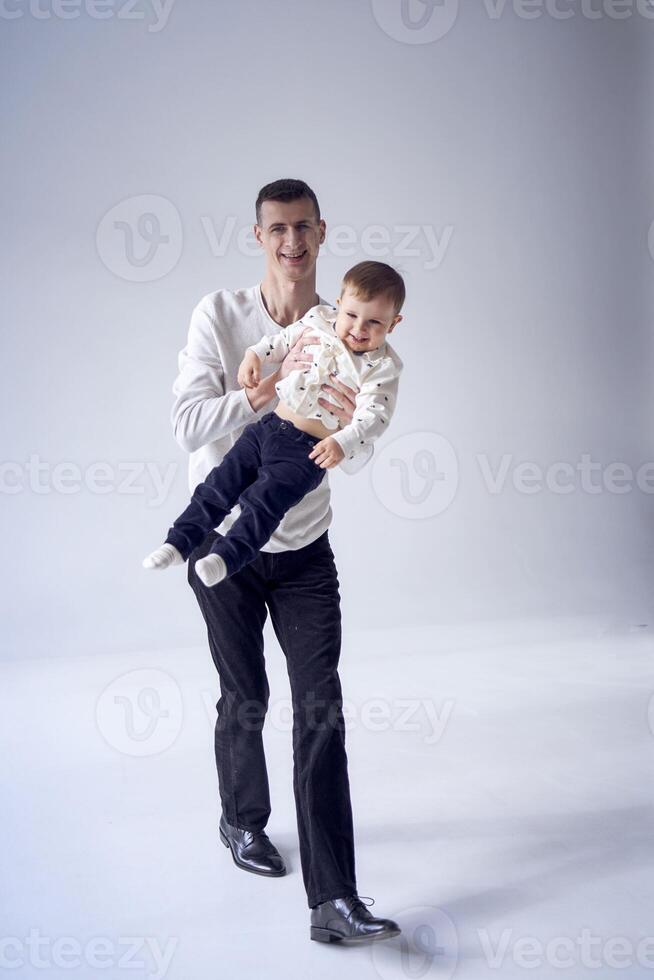 ein Vater trägt seine Sohn im seine Waffen und Theaterstücke mit ihm im ein minimalistisch Studio foto