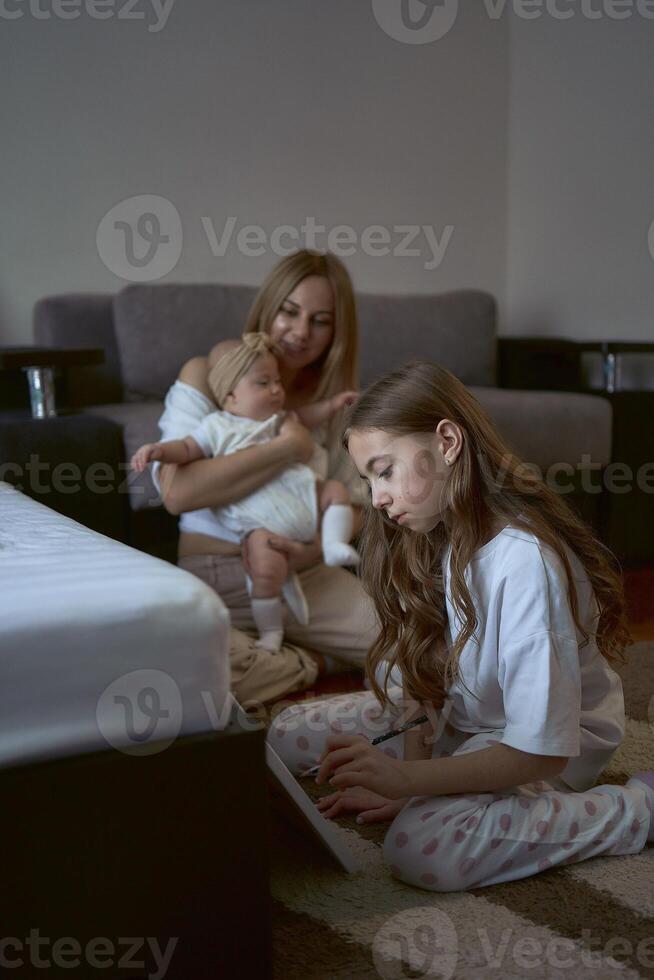 Mädchen Farbe auf das Fußboden während ihr Mutter Theaterstücke mit Baby Schwester foto