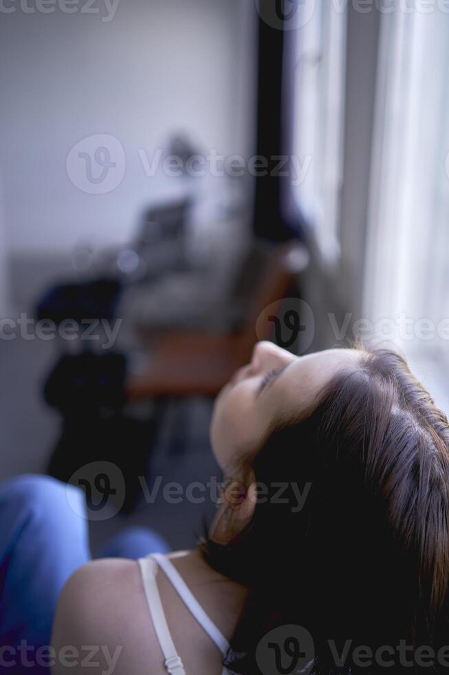 jung Teenager Mädchen Kampf Gehirn Krebs im ein Studio Foto schießen Sitzung auf ein Stuhl durch das Fenster