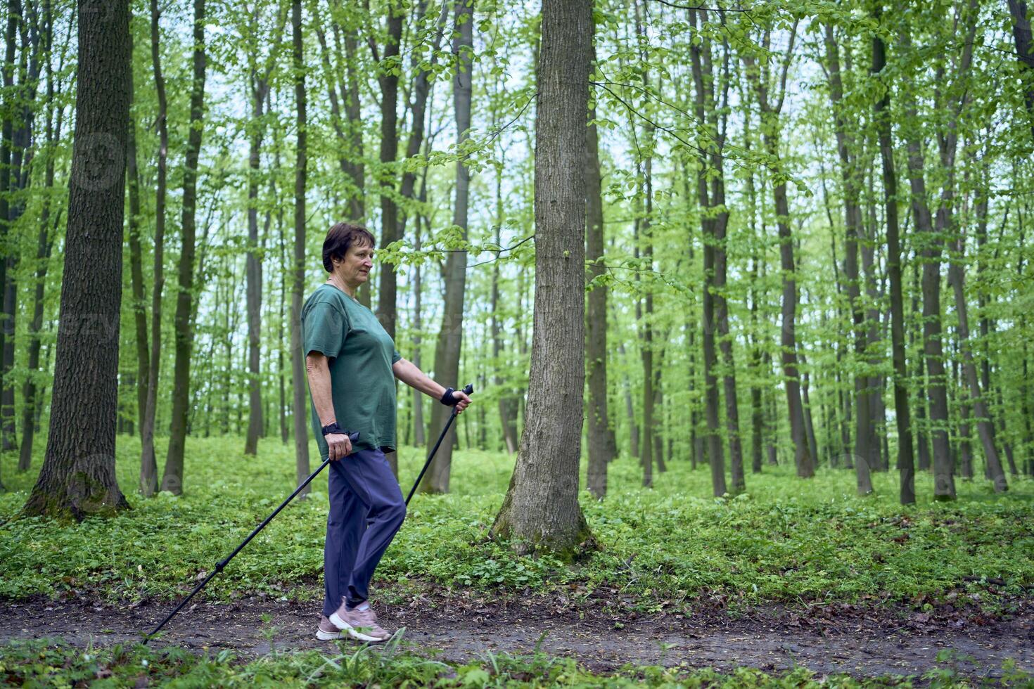 Alten Frau ist beschäftigt, verlobt im nordisch Gehen mit Stöcke im das Frühling Wald foto