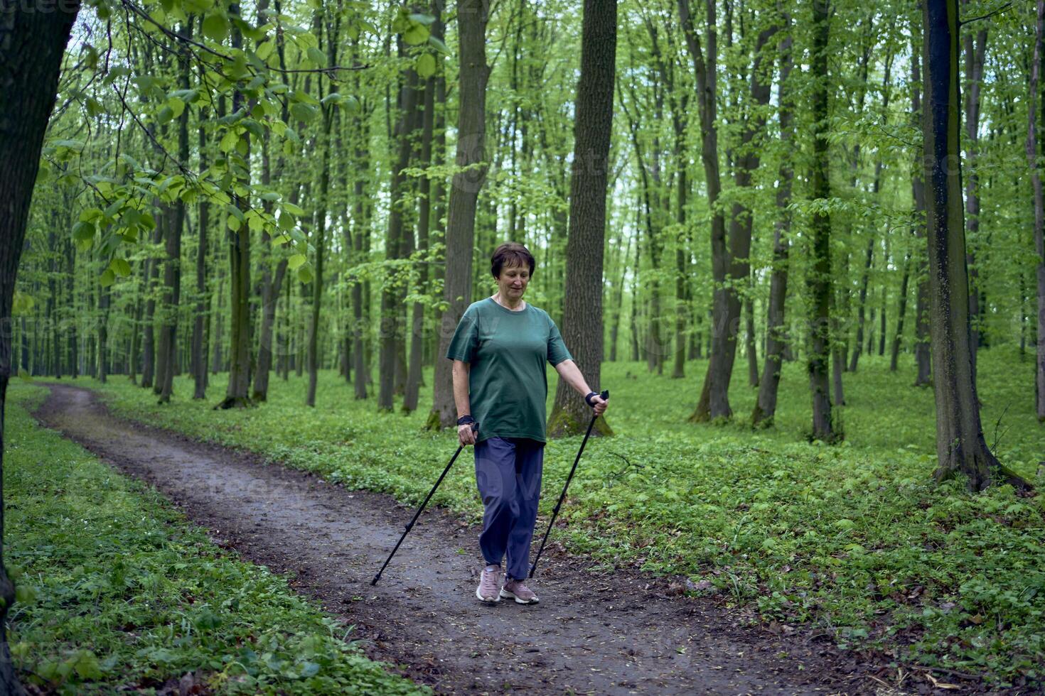 Alten Frau ist beschäftigt, verlobt im nordisch Gehen mit Stöcke im das Frühling Wald foto