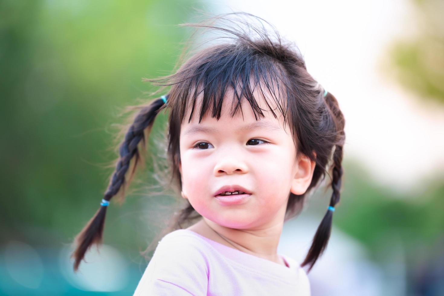 Kopfschuss. glückliches süßes Kind süßes Lächeln. asiatisches Mädchen flechten zwei Zöpfe. Naturhintergrund verwischen. im Sommer oder Frühling. Kind im Alter von 4 Jahren, das ein weiches rosa Hemd trägt. foto