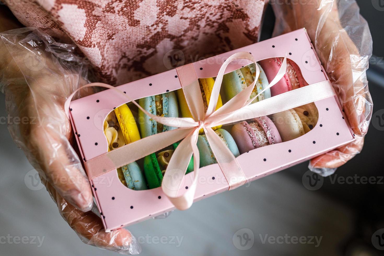 Mädchen in Schutzhandschuhen hält ein Paket hausgemachter Macarons als Geschenk foto