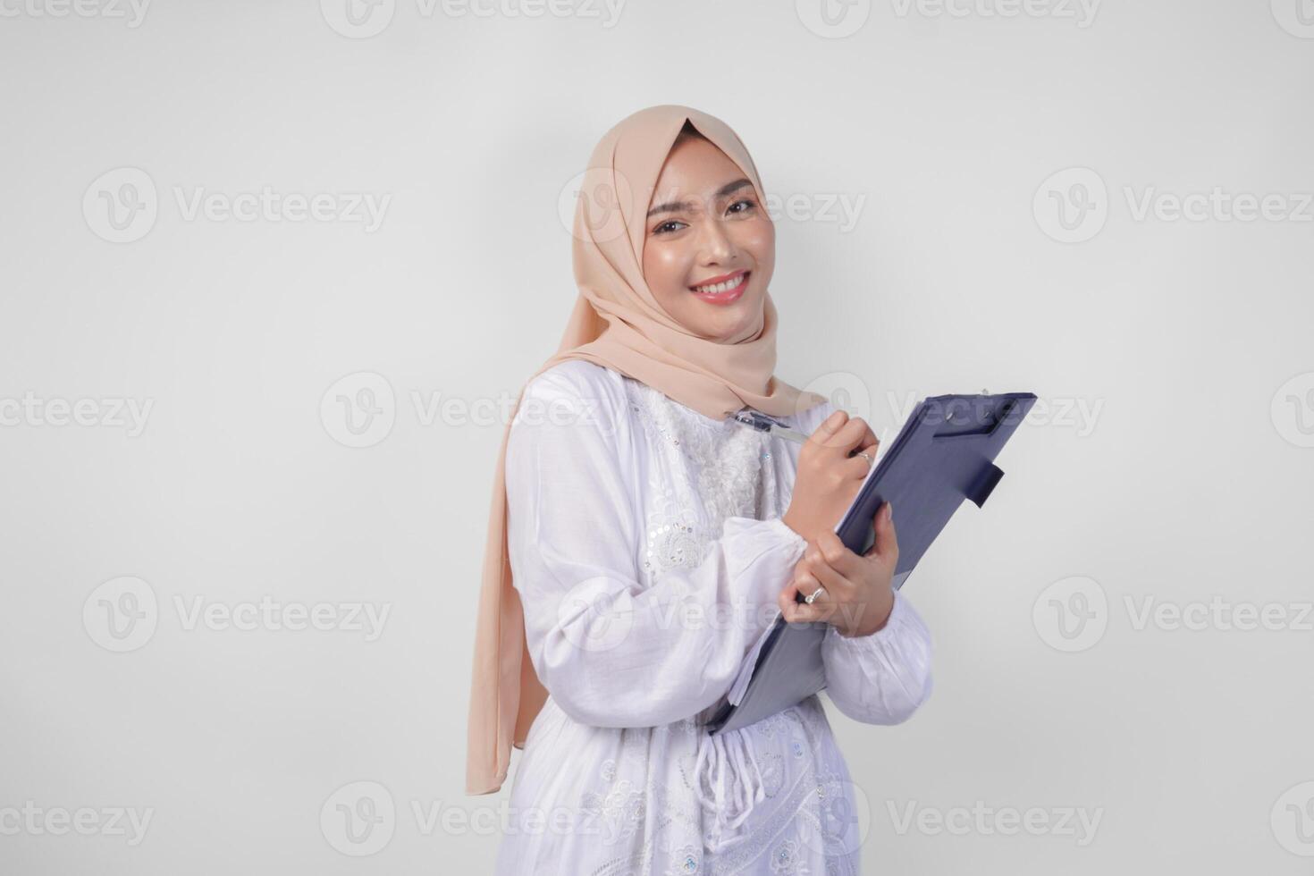 lächelnd jung asiatisch Muslim Frau tragen Weiß Kleid und Hijab halten ein dokumentieren, isoliert durch Weiß Hintergrund. Ramadan und eid Mubarak Konzept foto