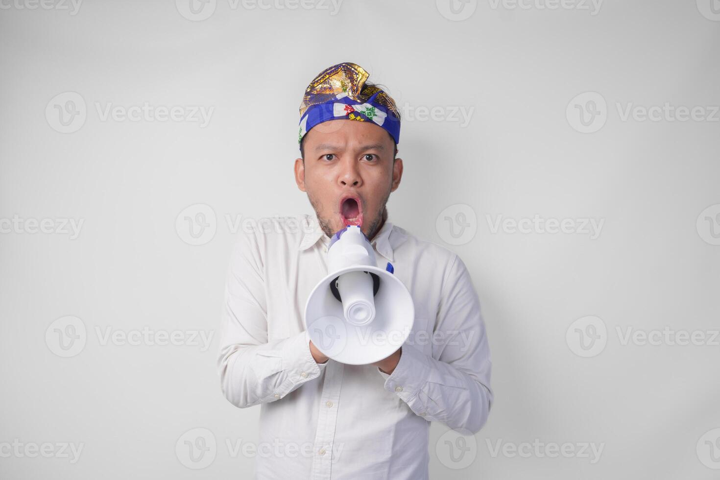 überglücklich balinesisch Mann im Weiß Hemd und traditionell Kopfschmuck schreien beim Megaphon Gefühl aufgeregt, isoliert durch Weiß Hintergrund foto
