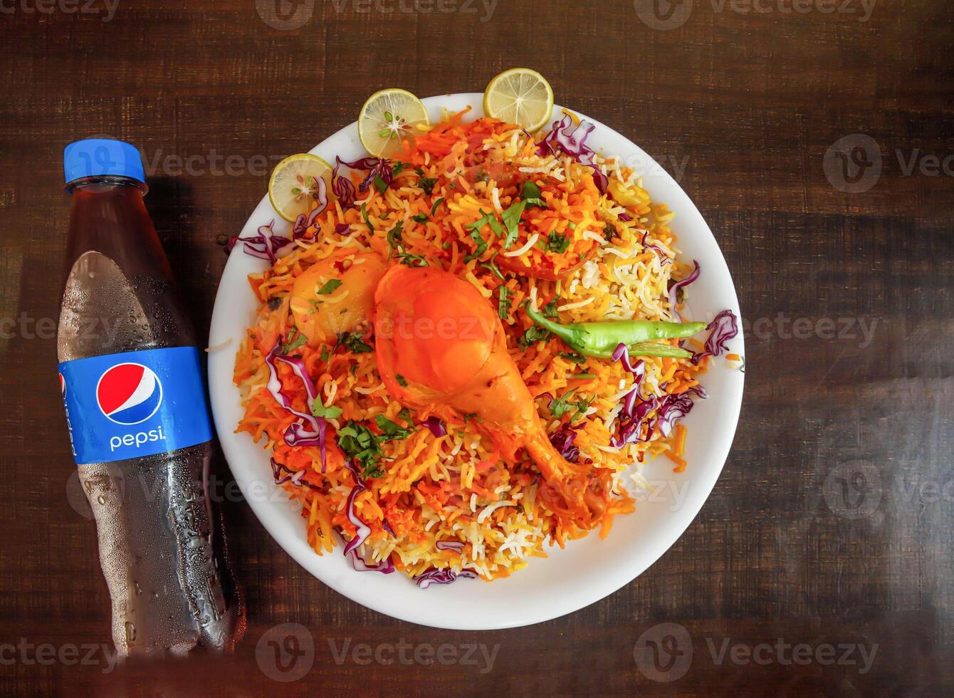 würzig Hähnchen Biryani mit Kartoffel, Pepsi Flasche 345 ml, Zwiebel und Zitrone Scheibe serviert im Teller isoliert hölzern Hintergrund oben Aussicht indisch Gewürze und pakistanisch Essen foto