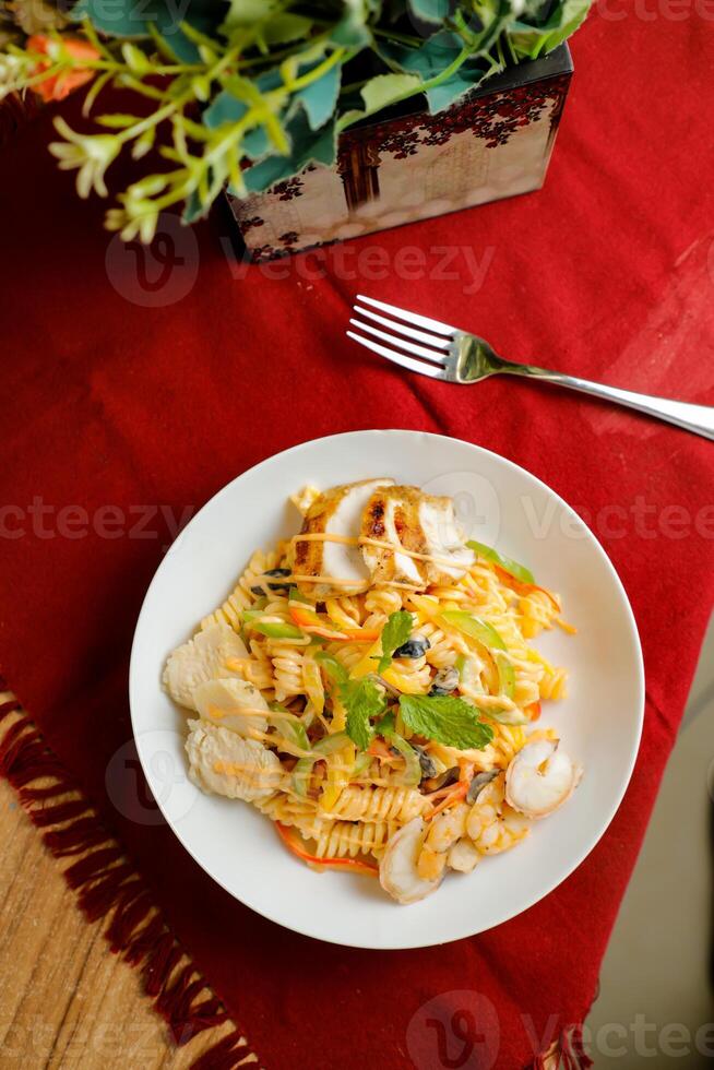 tropisch Pasta Salat mit mischen Fleisch Olive mit Garnele und Garnele serviert im Schüssel mit Blumen und Gabel isoliert auf rot Serviette oben Aussicht von gesund Grün Essen auf Tabelle foto