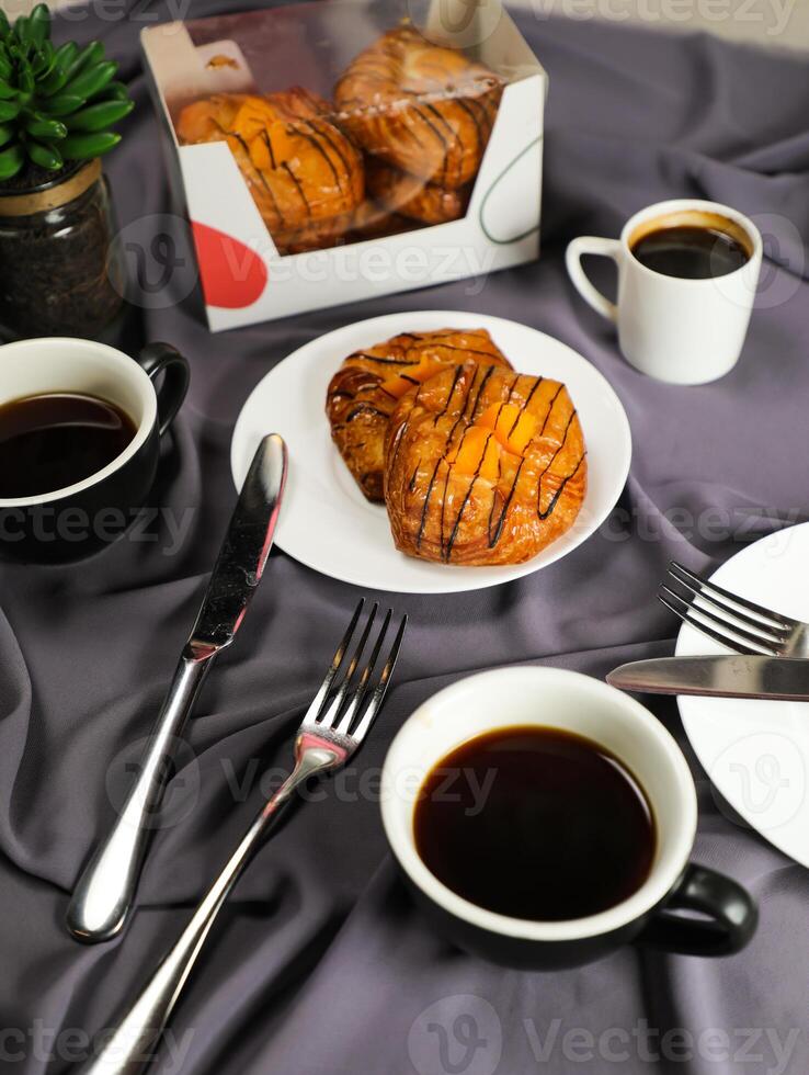 Pfirsich dänisch Gebäck Puff serviert im Teller mit Tasse von schwarz Kaffee isoliert auf Serviette mit Gabel und Messer oben Aussicht von Französisch Frühstück gebacken Essen Artikel auf grau Hintergrund foto