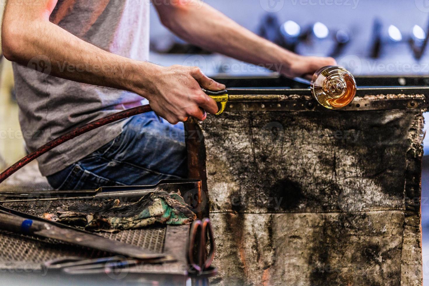 Mannhände Nahaufnahme, die an einem mundgeblasenen Glasstück arbeiten foto