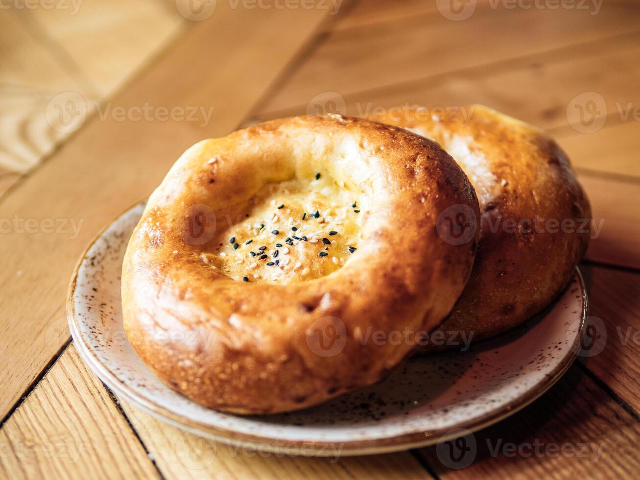 lecker frisch Tandoor Brot auf rustikal hölzern Tischplatte. zwei Tandoor eben Brot Kuchen mit schwarz Sesam Saat auf Gelb hölzern Tabelle Hintergrund. National asiatisch Mahlzeit und Essen foto