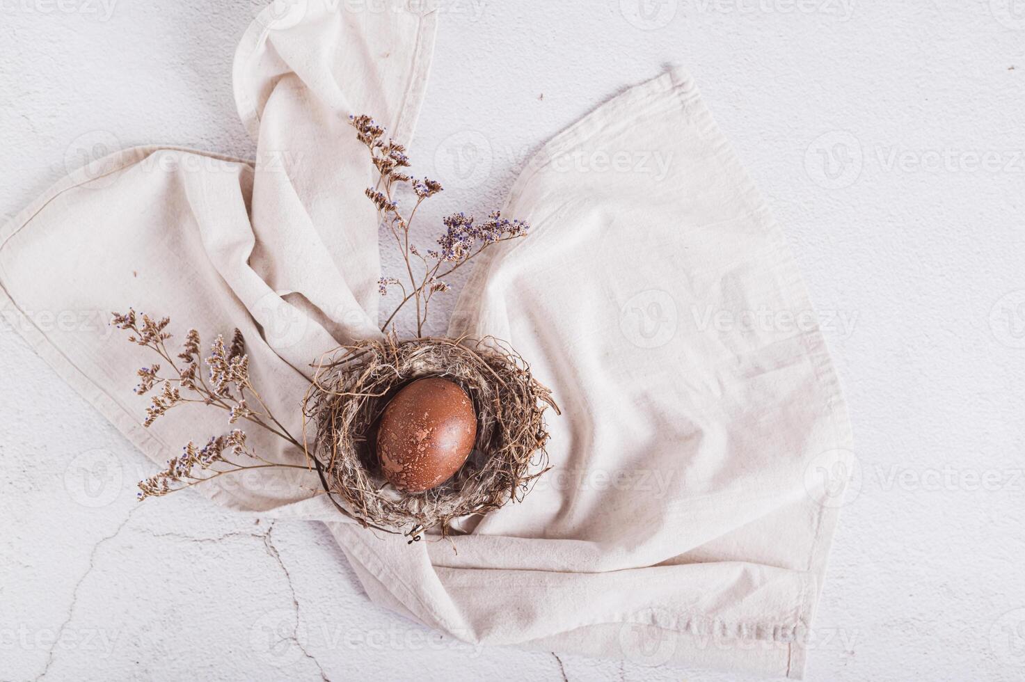 hausgemacht natürlich farbig Ei im ein Nest auf ein Serviette und getrocknet Blumen auf das Tabelle oben Aussicht foto