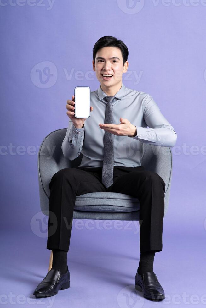 Porträt von asiatisch Geschäft Mann Sitzung auf Sofa, isoliert auf lila Hintergrund foto