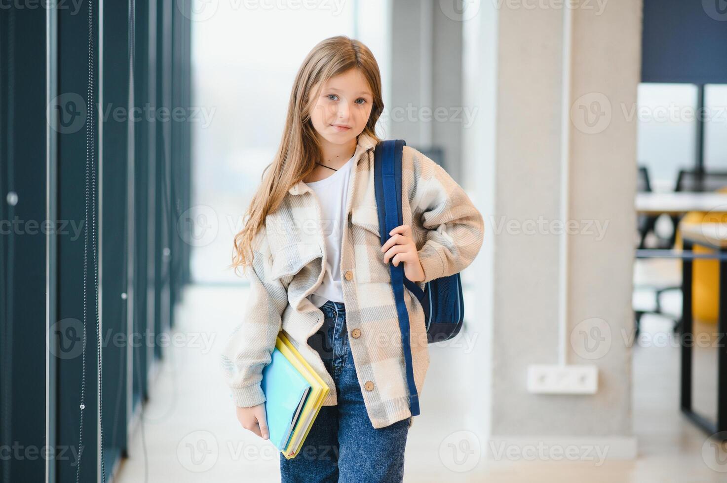 wenig schön Schule Mädchen Stehen unter Gang beim Schule, halten Anmerkungen beim Hände. komisch und glücklich Mädchen lächelnd beim Kamera, ruhen nach Lektionen auf primär Schule foto