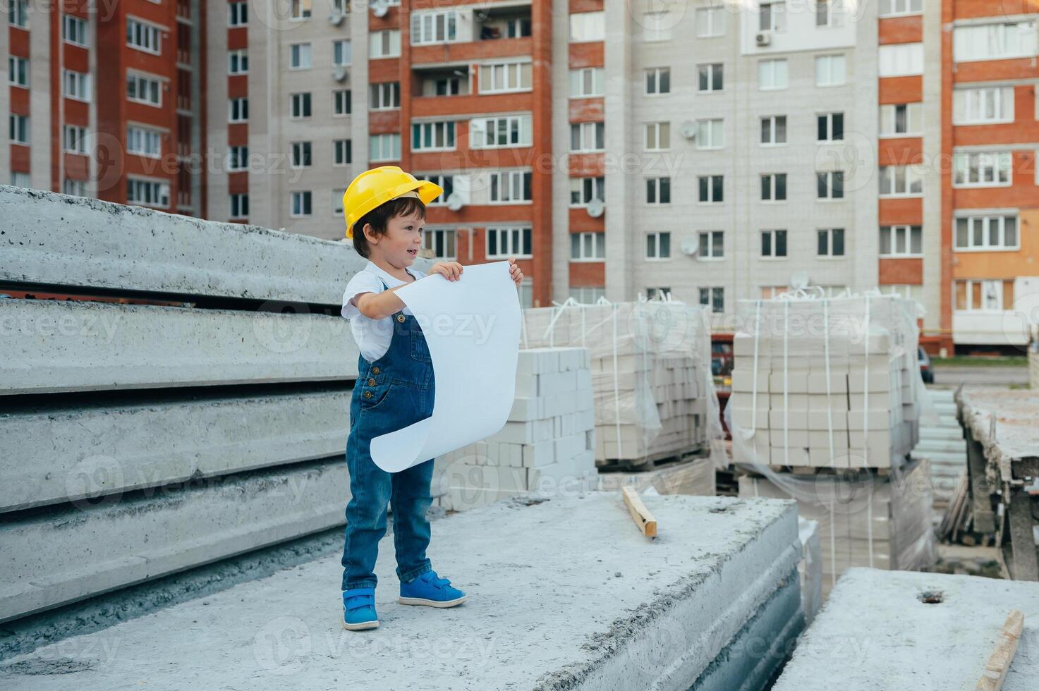 Architekt im Helm Schreiben etwas in der Nähe von Neu Gebäude. wenig süß Junge auf das Gebäude wie ein Architekt foto