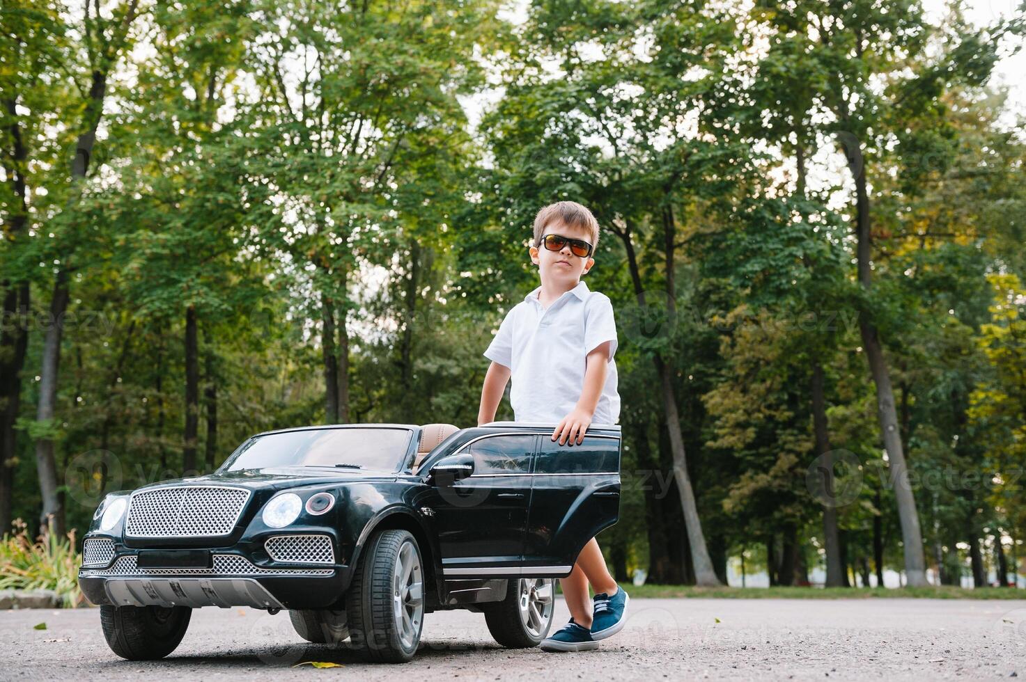 süß Junge im Reiten ein schwarz elektrisch Auto im das Park. komisch Junge Fahrten auf ein Spielzeug elektrisch Wagen. Kopieren Raum. foto