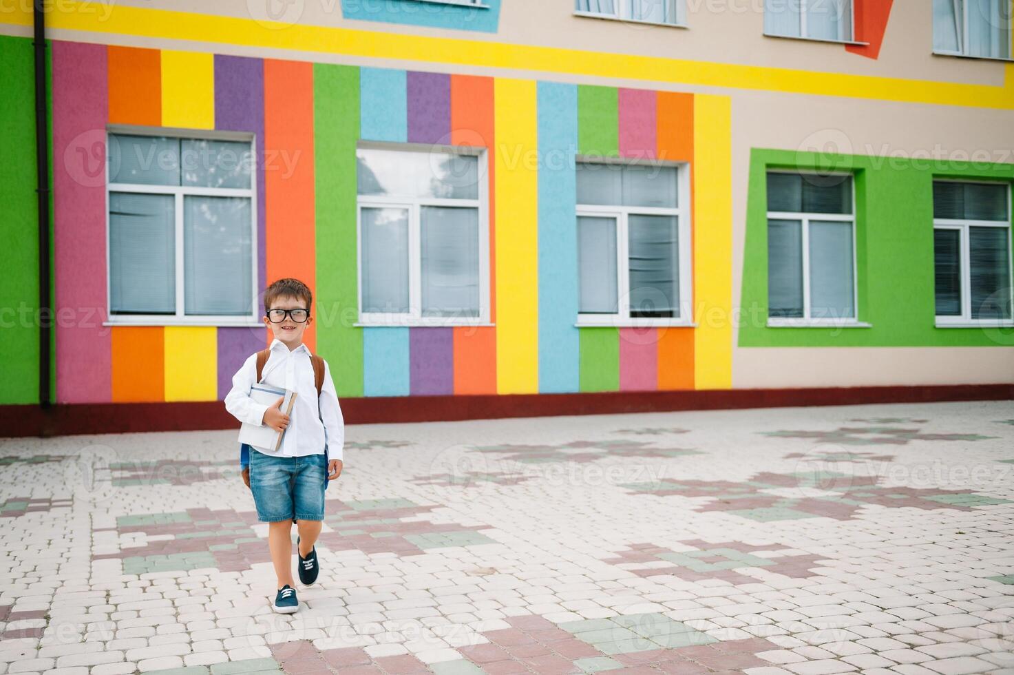 zurück zu Schule. glücklich lächelnd Junge im Brille ist gehen zu Schule zum das zuerst Zeit. Kind mit Rucksack und Buch draußen. Anfang von Unterricht. zuerst Tag von fallen. foto