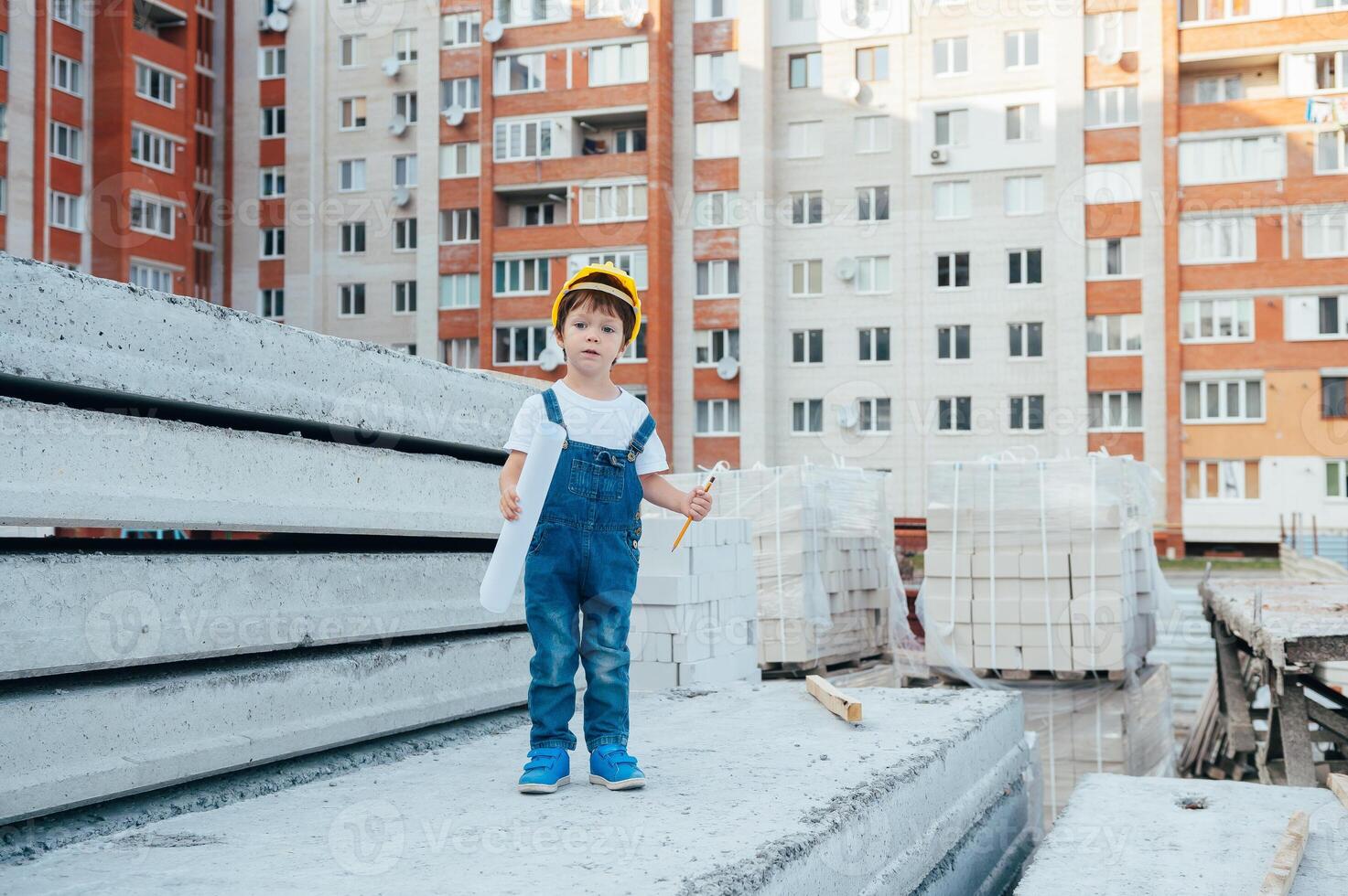 Architekt im Helm Schreiben etwas in der Nähe von Neu Gebäude. wenig süß Junge auf das Gebäude wie ein Architekt foto