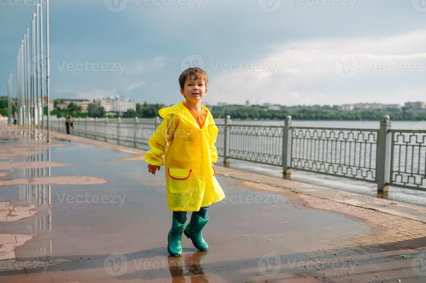 wenig Junge spielen im regnerisch Sommer- Park. Kind mit Regenschirm, wasserdicht Mantel und Stiefel Springen im Pfütze und Schlamm im das Regen. Kind Gehen im Sommer- Regen draussen Spaß durch irgendein Wetter. glücklich Kindheit. foto