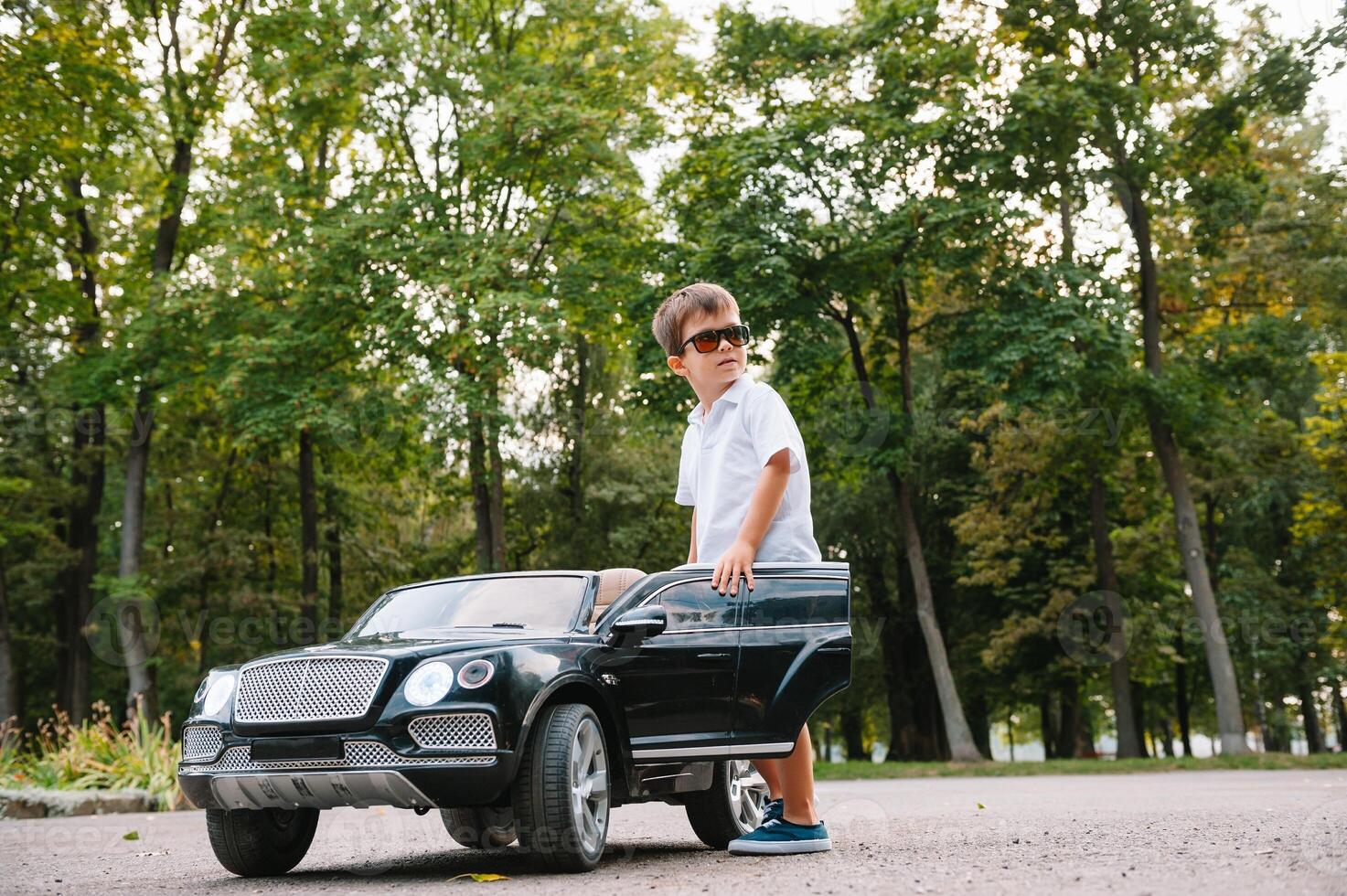 süß Junge im Reiten ein schwarz elektrisch Auto im das Park. komisch Junge Fahrten auf ein Spielzeug elektrisch Wagen. Kopieren Raum. foto