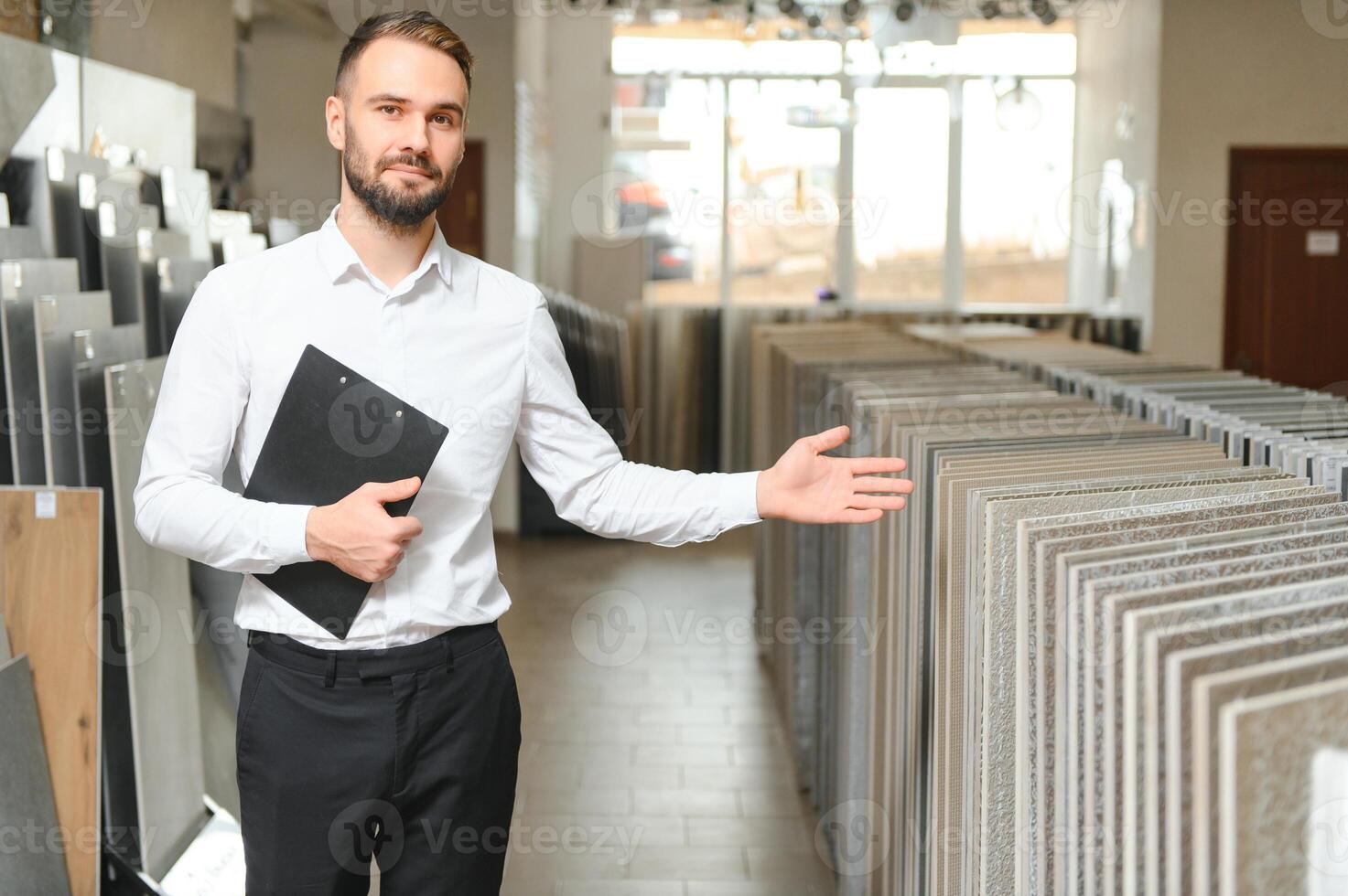 Porträt von ein Keramik Fliese Verkäufer. das Verkäufer steht gegen das Hintergrund von ein groß Sortiment von Fliesen foto