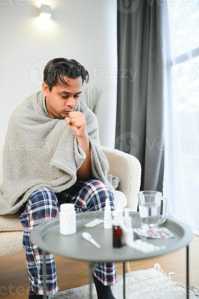 krank indisch Mann im Plaid sitzen allein Zittern von kalt. ungesund arabisch Kerl sitzen auf Stuhl Gefühl Beschwerden Versuchen zu Erwärmen oben foto