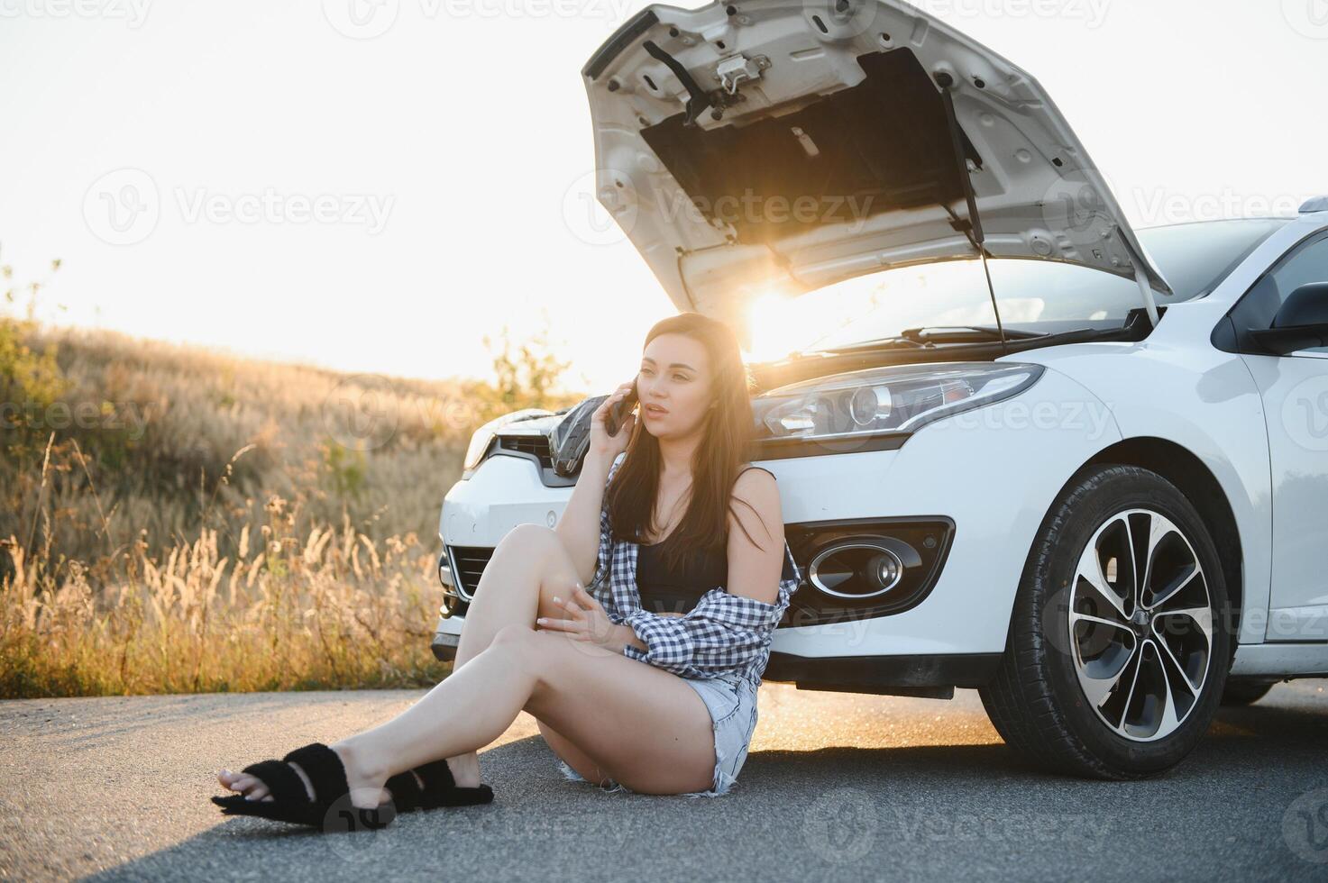 schön jung Mädchen Sitzung beim ein gebrochen Auto auf das Straße verzweifelt zu erhalten Hilfe foto