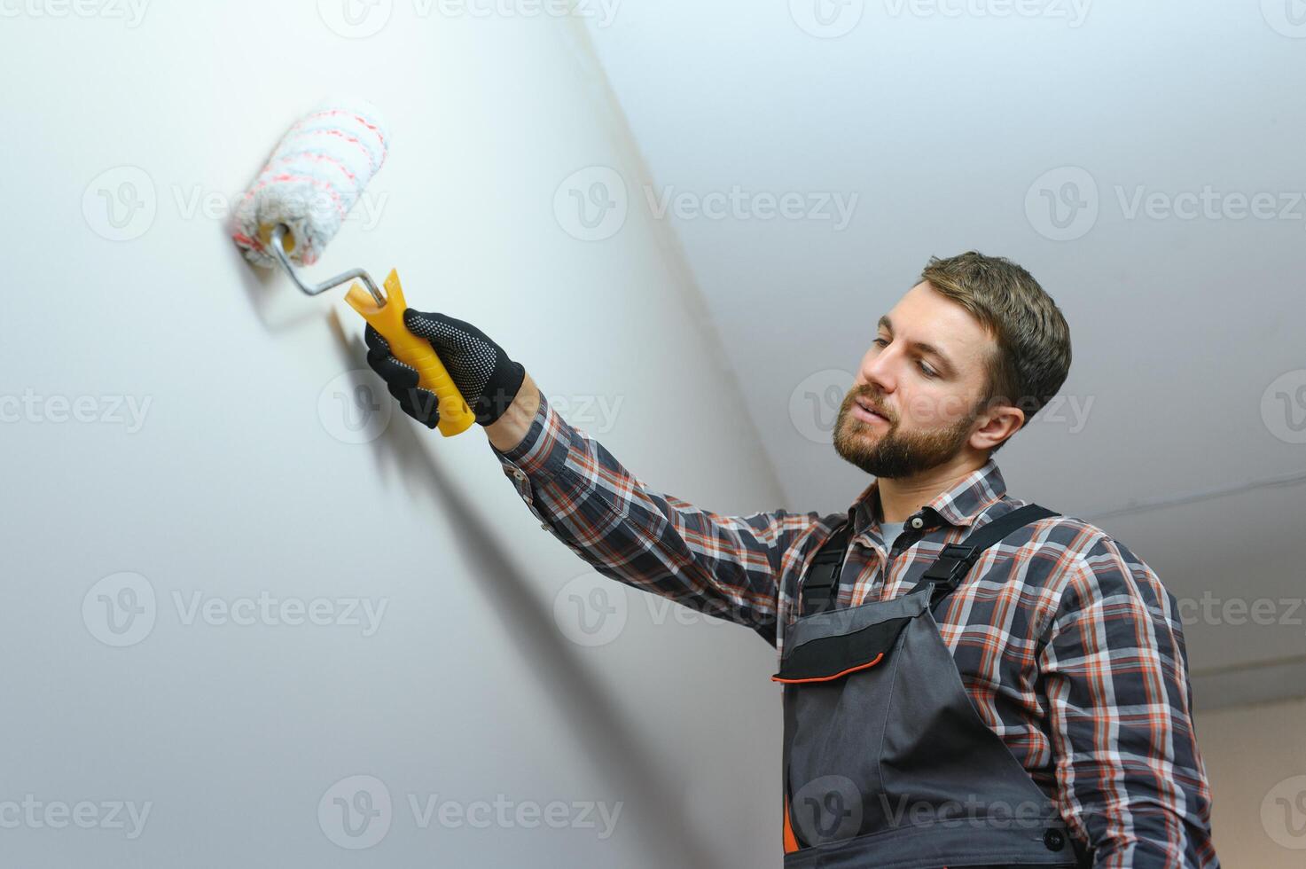 Maler Gemälde ein Mauer mit Farbe Rolle. Baumeister Arbeiter Gemälde Oberfläche mit Weiß Farbe foto