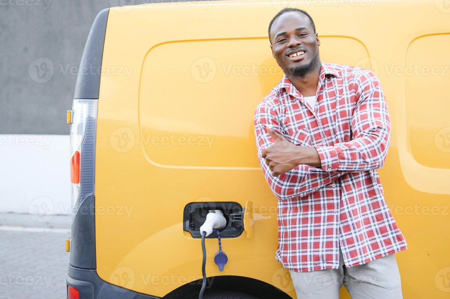ein afrikanisch amerikanisch Mann steht Nächster zu Gelb elektrisch Lieferung van beim elektrisch Fahrzeug Laden Stationen foto