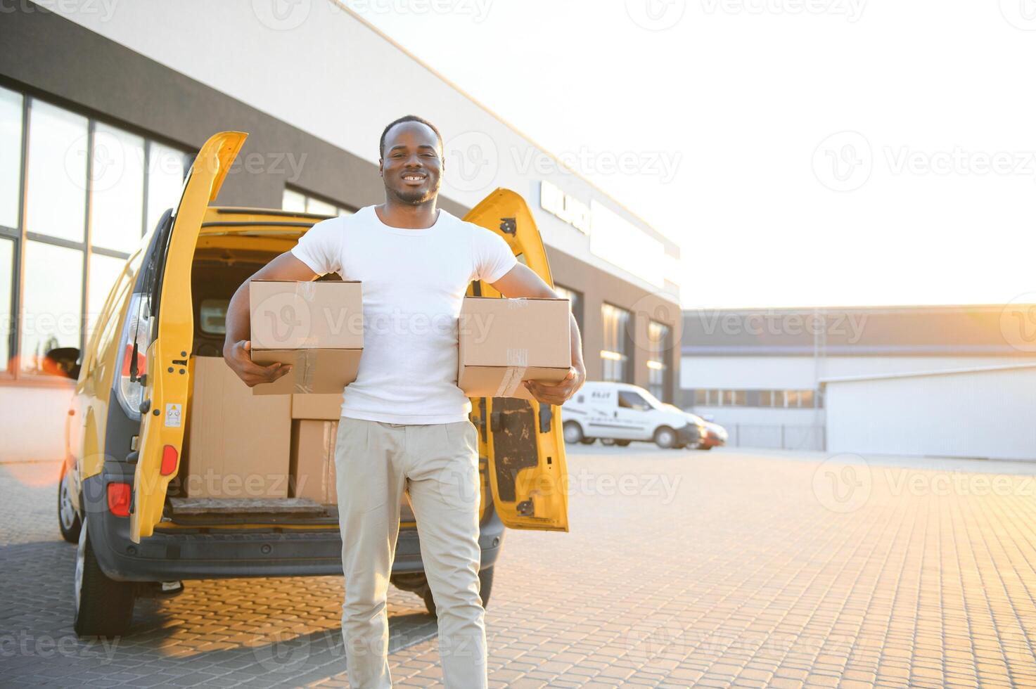 Porträt von ein jung afrikanisch amerikanisch Paket Lieferung Mann in der Nähe von ein Auto mit Boxen. foto