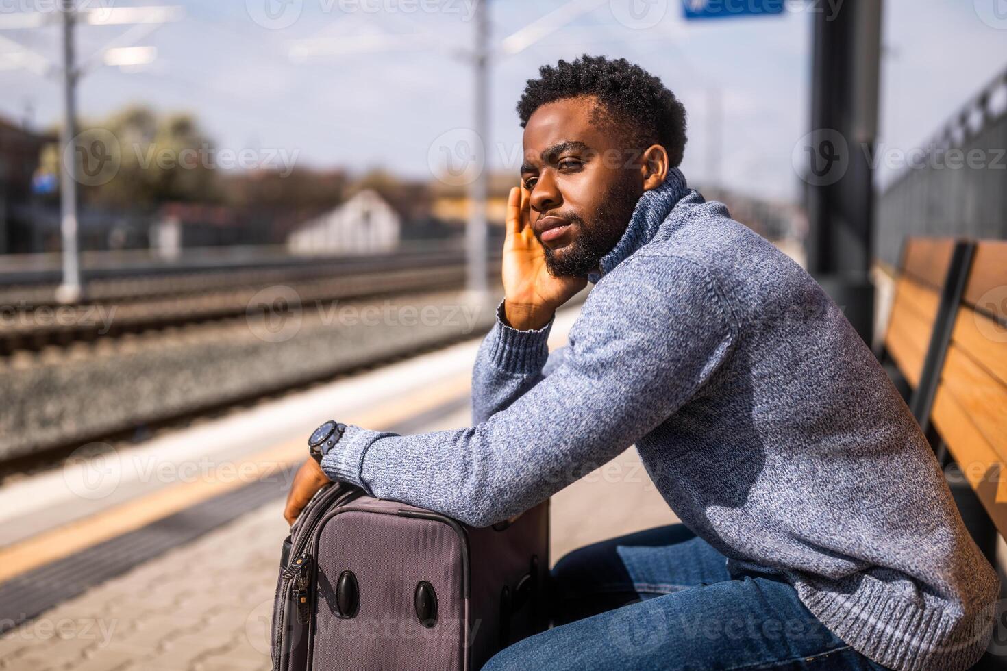 besorgt Mann mit ein Koffer Sitzung auf ein Bank beim das Eisenbahn Bahnhof. foto