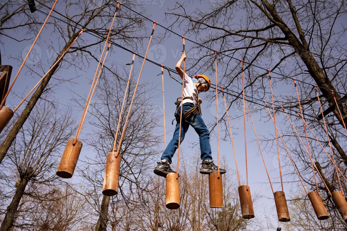 ein Junge im ein Helm klettert ein Seil Park im das Frühling foto