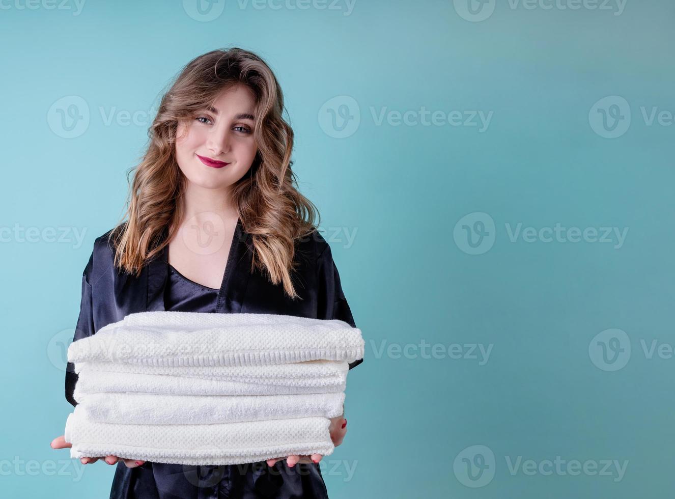 glückliche Hausfrau, die einen Haufen sauberer weißer Handtücher auf blauem Hintergrund hält foto