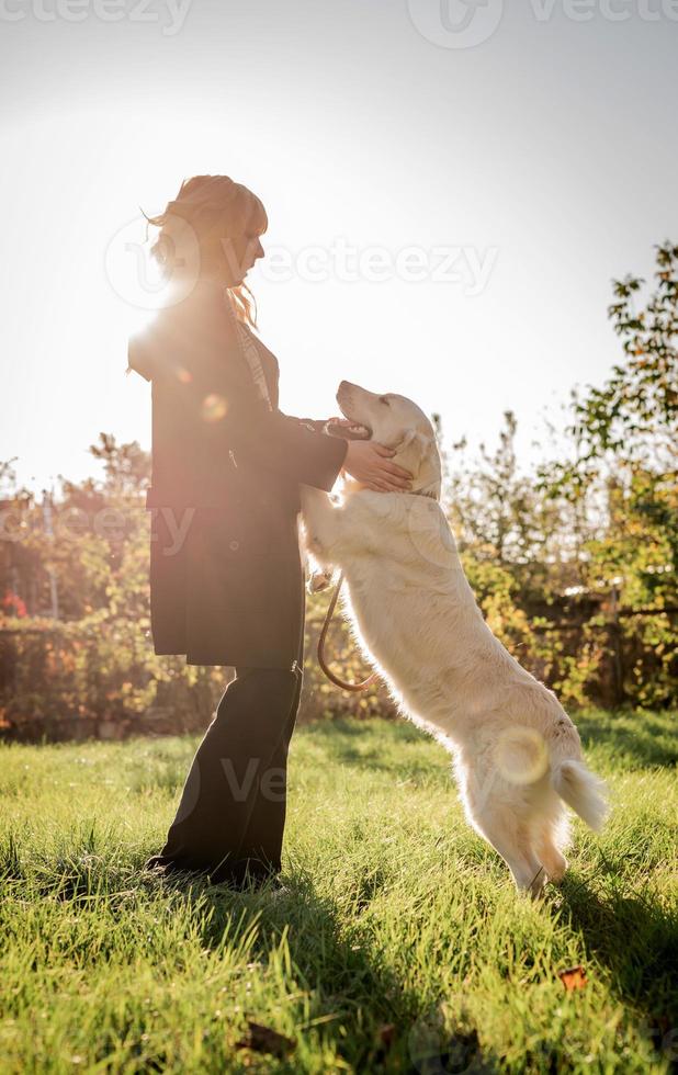 schöne kaukasische Frau, die mit ihrem goldenen Labrador Retriever Hund in einem Park im Sonnenuntergang spielt foto