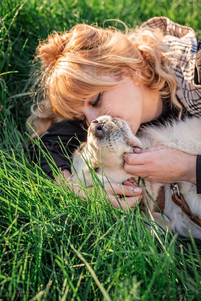 Schöne kaukasische Frau, die mit ihrem goldenen Labrador Retriever-Hund in einem Park im Sonnenuntergang im Gras liegt? foto