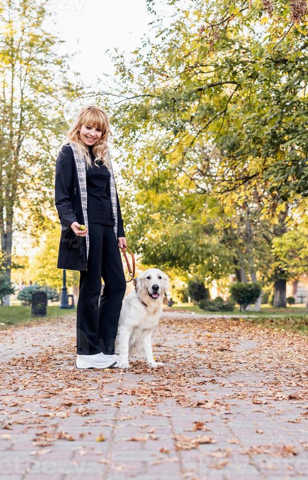 glückliche kaukasische Frau mit ihrem Retriever-Hund, die in einem Herbstpark spazieren geht foto