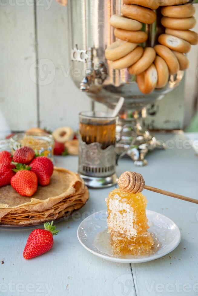 immer noch Leben im das Russisch Tradition zum Maslenitsa, Pfannkuchen mit Honig und Erdbeeren, Tee von ein Samowar mit Bagels foto