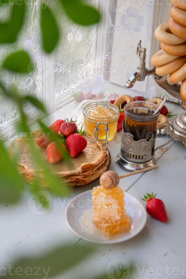 immer noch Leben im das Russisch Tradition zum Maslenitsa, Pfannkuchen mit Honig und Erdbeeren, Tee von ein Samowar mit Bagels foto