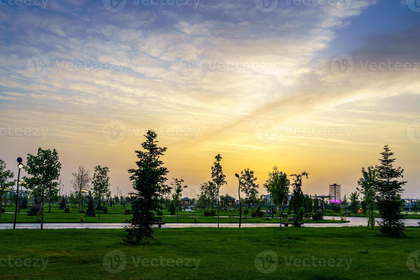 Stadt Park im früh Sommer- oder Frühling mit Laternen, jung Grün Rasen, Bäume und dramatisch wolkig Himmel auf ein Sonnenuntergang oder Sonnenaufgang. foto