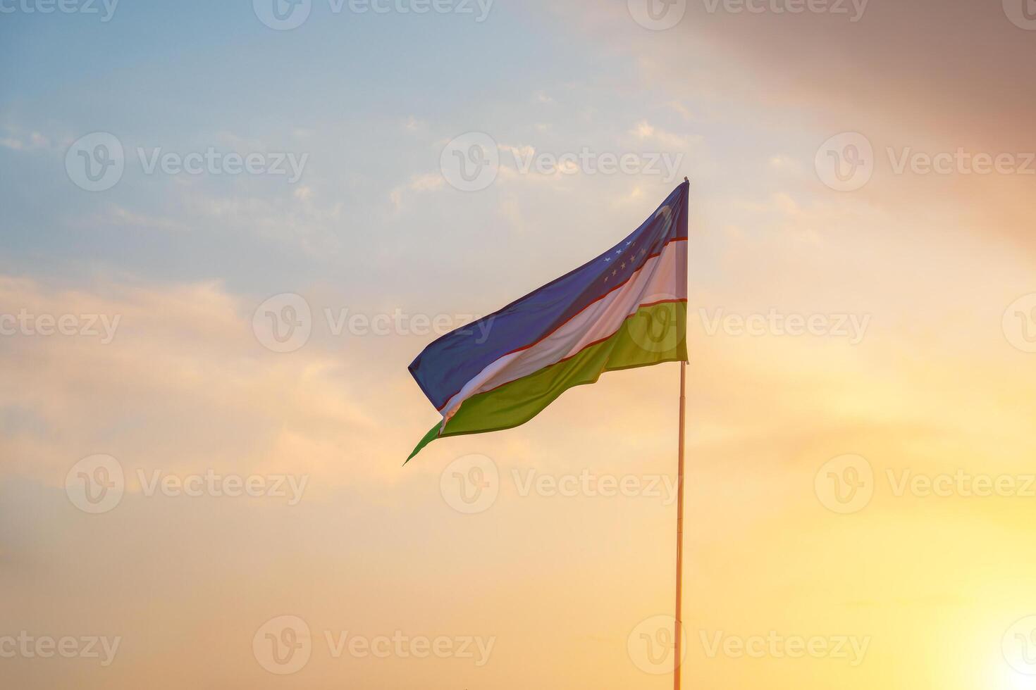 Flagge von Usbekistan winken auf ein Sonnenuntergang oder Sonnenaufgang dramatisch Himmel Hintergrund. foto