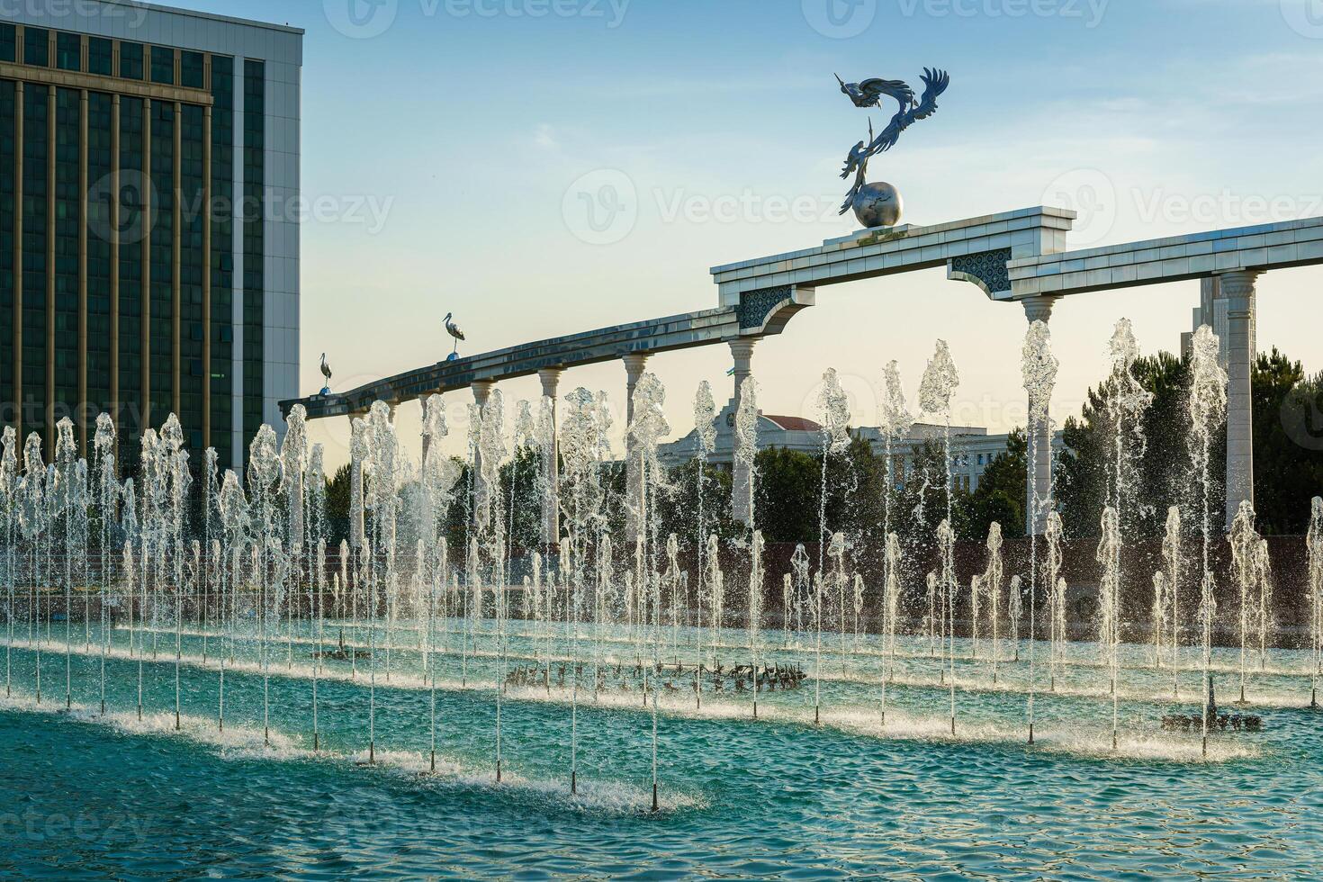 Denkmal und Reihen von Brunnen beleuchtet durch Sonnenlicht beim Sonnenuntergang oder Sonnenaufgang im das Unabhängigkeit Platz beim Sommer, Taschkent. foto